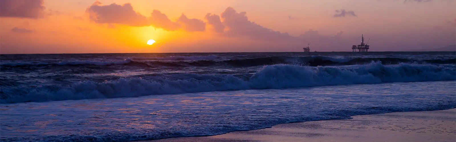 Image of a sunset over the ocean, with an offshore oil platform in the background.