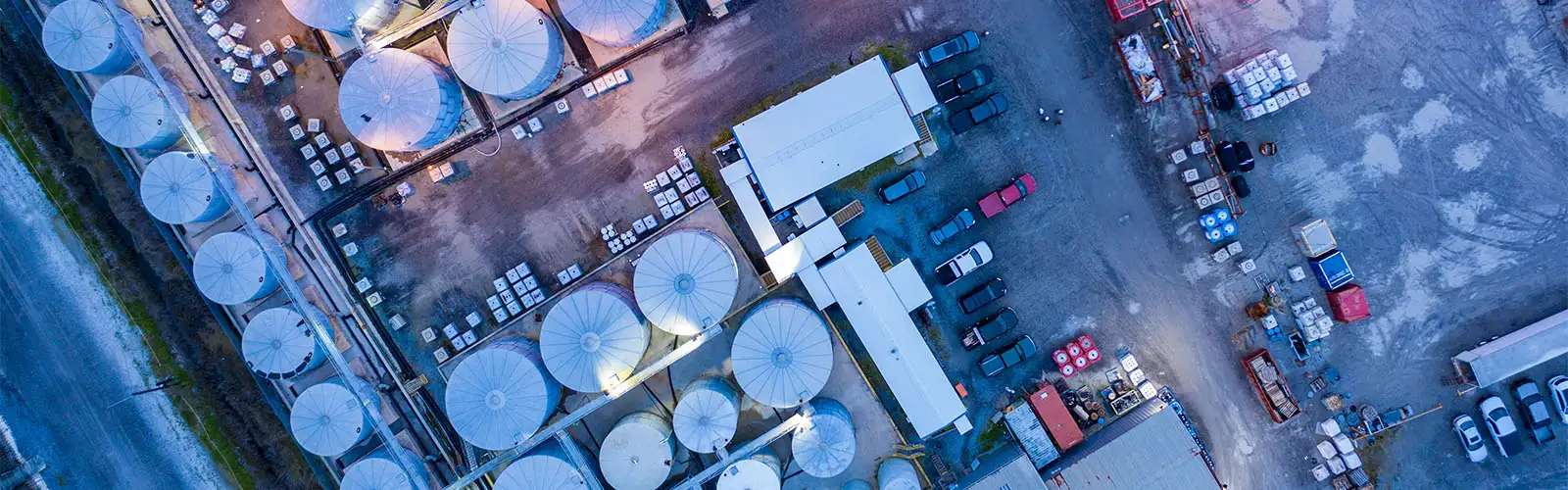 Vista aérea de una instalación con grandes tanques cilíndricos de almacenamiento, edificios, contenedores y vehículos estacionados.