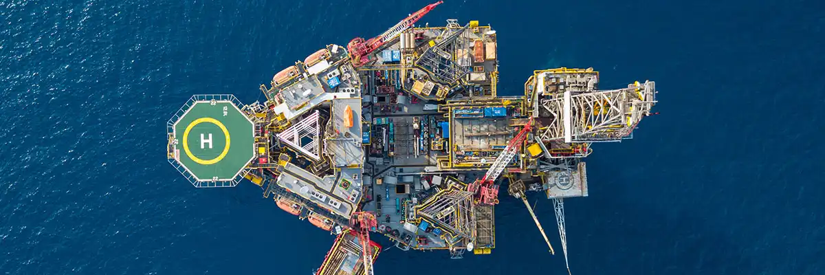 Vista aérea de una plataforma petrolífera en alta mar situada en aguas de un azul intenso, con un helipuerto.