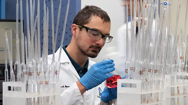 Un empleado de TETRA con gafas de seguridad, guantes azules y bata de laboratorio, sosteniendo un vaso de precipitados con un líquido rojo en un laboratorio.