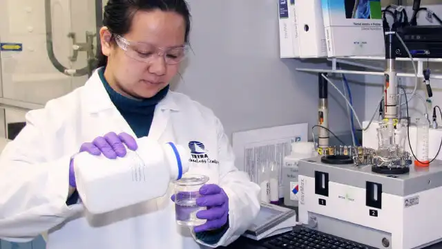 Un empleado de TETRA que trabaja en un laboratorio, mientras vierte un líquido transparente en un vaso de precipitados desde un recipiente blanco.