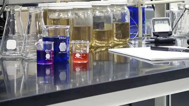 Puesto de trabajo de laboratorio en el que se muestran recipientes de vidrio de distintos tamaños, con y sin líquidos de colores.