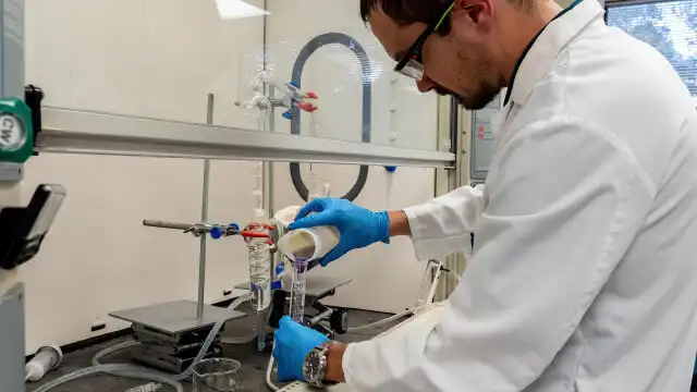 En TETRA-anställd som utför kemiska tester för vattenhantering i en laboratoriemiljö, iklädd blå handskar, labbrock och skyddsglasögon.