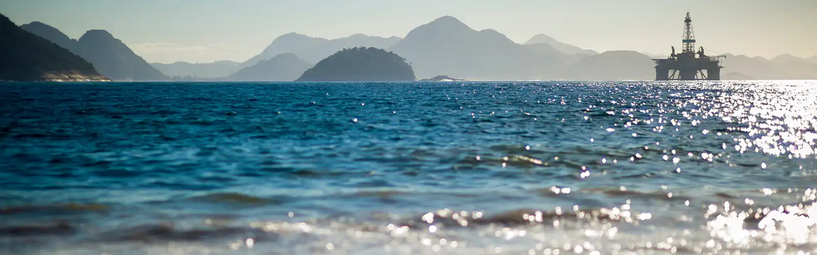 Una plataforma petrolífera en alta mar con altas montañas al fondo.