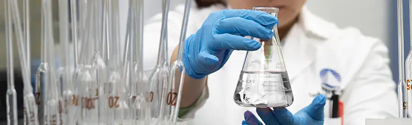 TETRA-anställd arbetar i ett laboratorium, bär blå handskar och håller en glaskolv i båda händerna.