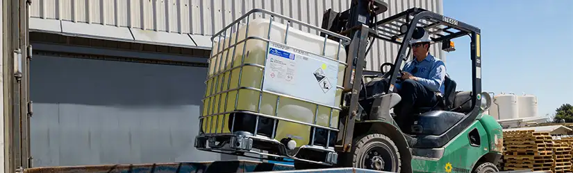 A TETRA employee operating a forklift, transporting a container of fluid.