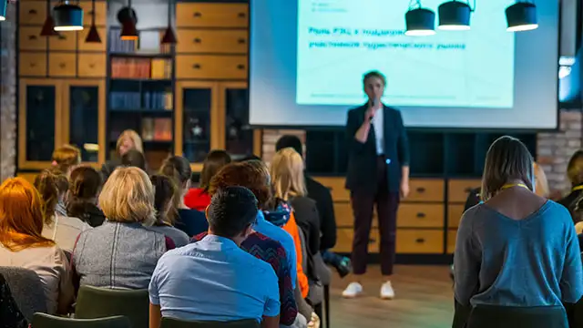 Kvinnlig affärsman presenterar för en publik med en bildpresentation på en skärm bakom henne.
