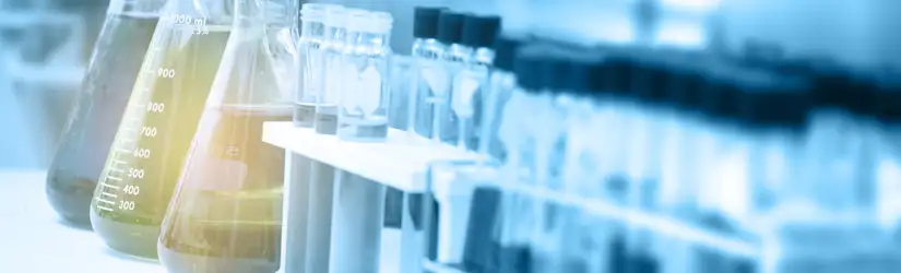 A laboratory displaying clear glassware, including flasks with measurement markings on the side containing liquids, by a set of small test tubes.