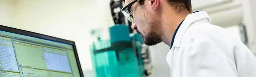 A employee sitting in a laboratory, while staring at a monitor with data.