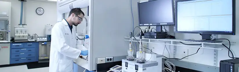 En man iförd labbrock, blå handskar och skyddsglasögon utför forskning i ett laboratorium.
