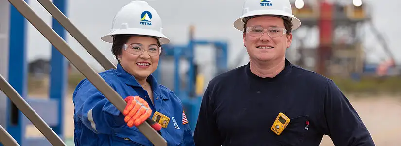 Två TETRA-anställda ler med skyddshjälmar på en arbetsplats.