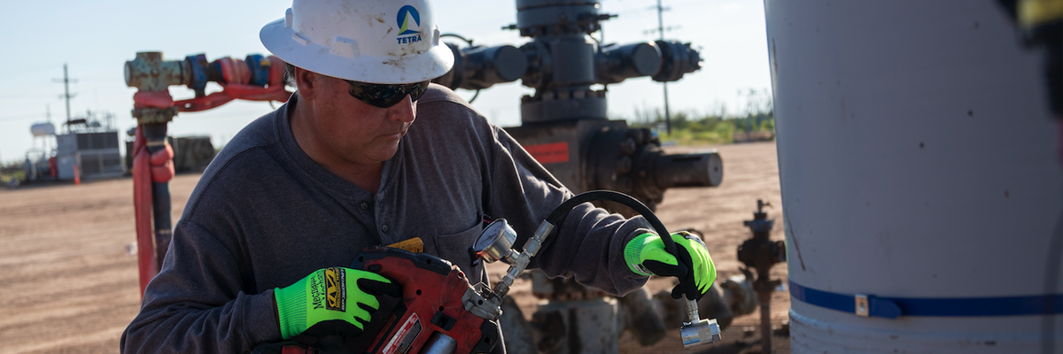 Trabajador que lleva guantes de alta visibilidad en las manos mientras maneja maquinaria en unas instalaciones de TETRA Energy Services.
